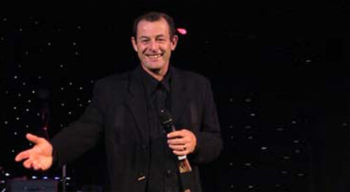 Micky Zany smiling whilst performing with a microphone in his hand